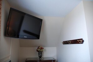 A room with a mounted television on the wall, a small table with a vase of flowers, and a coat rack with a single item. - Commons Inn (Halifax)