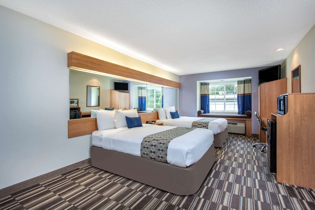 A hotel room with two beds, a large mirror, a television, and a window with curtains.