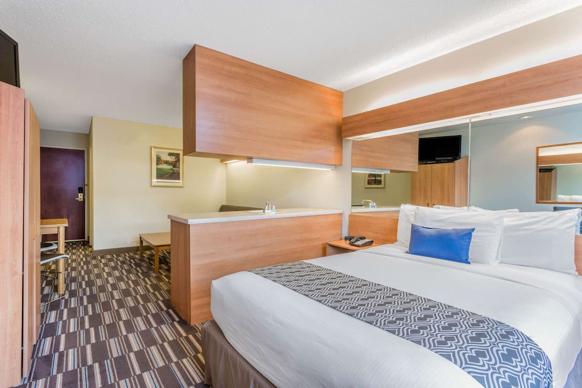 A hotel room with a large bed, a wooden desk, a mirror, and a television.