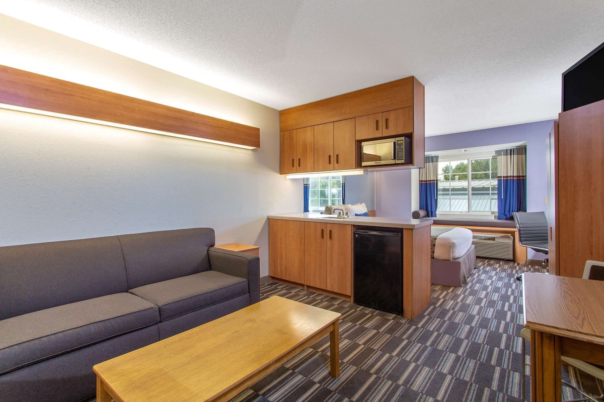 A compact room with a sofa, a small table, a kitchenette with a microwave, and a window with curtains.