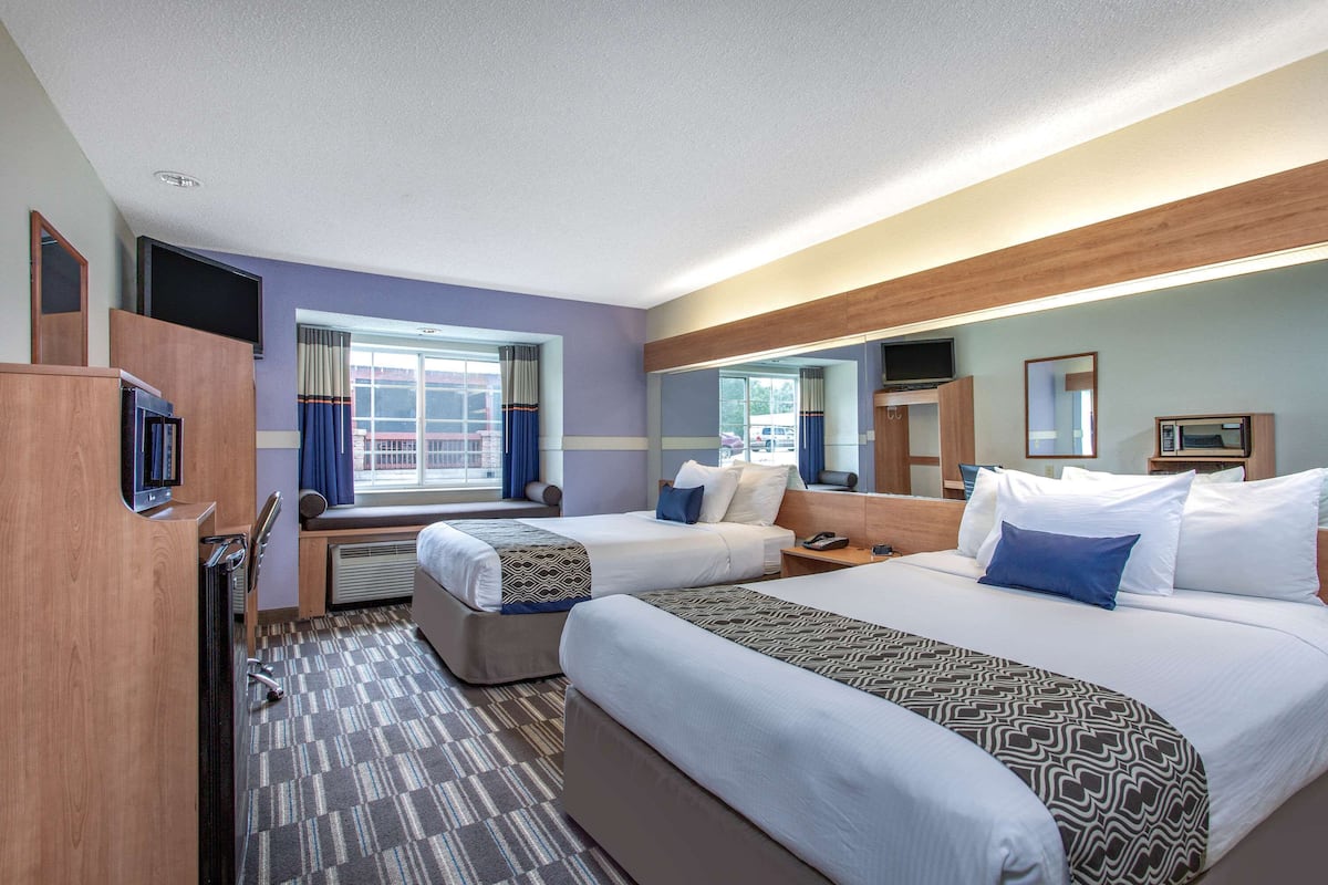 A hotel room with two beds, a TV, a desk, and a window with curtains.