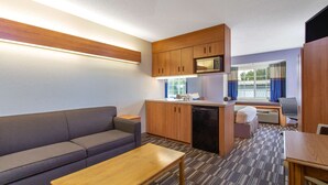 A compact room with a sofa, a wooden table, a kitchenette with a microwave, and a small window with curtains. - Microtel Inn & Suites by Wyndham Lillington / Campbell Univ (Lillington)