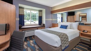 A hotel room with a large bed, a desk with a computer, a chair, a window with curtains, and a television. - Microtel Inn & Suites by Wyndham Lillington / Campbell Univ (Lillington)