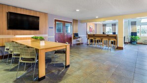 A modern hotel lobby with a wooden reception desk, a flat-screen TV, and a seating area with chairs and a small table. - Microtel Inn & Suites by Wyndham Lillington / Campbell Univ (Lillington)
