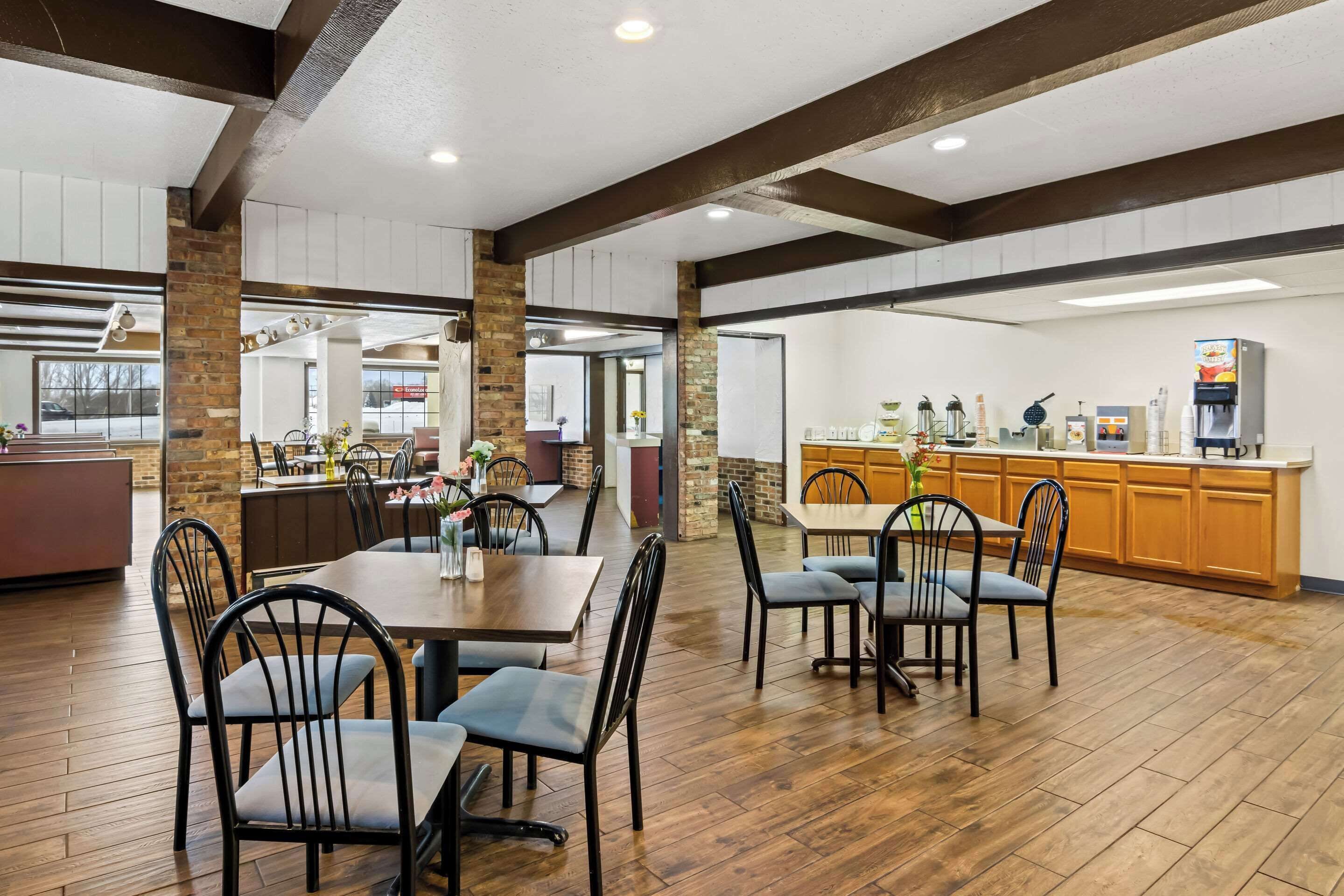 A spacious restaurant with wooden floors, brick pillars, and a central bar area.