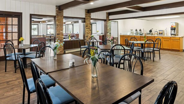 Un grand espace de salle à manger avec plusieurs tables et chaises, un coin cuisine équipé d’un espace pour préparer le café, et des murs en briques.