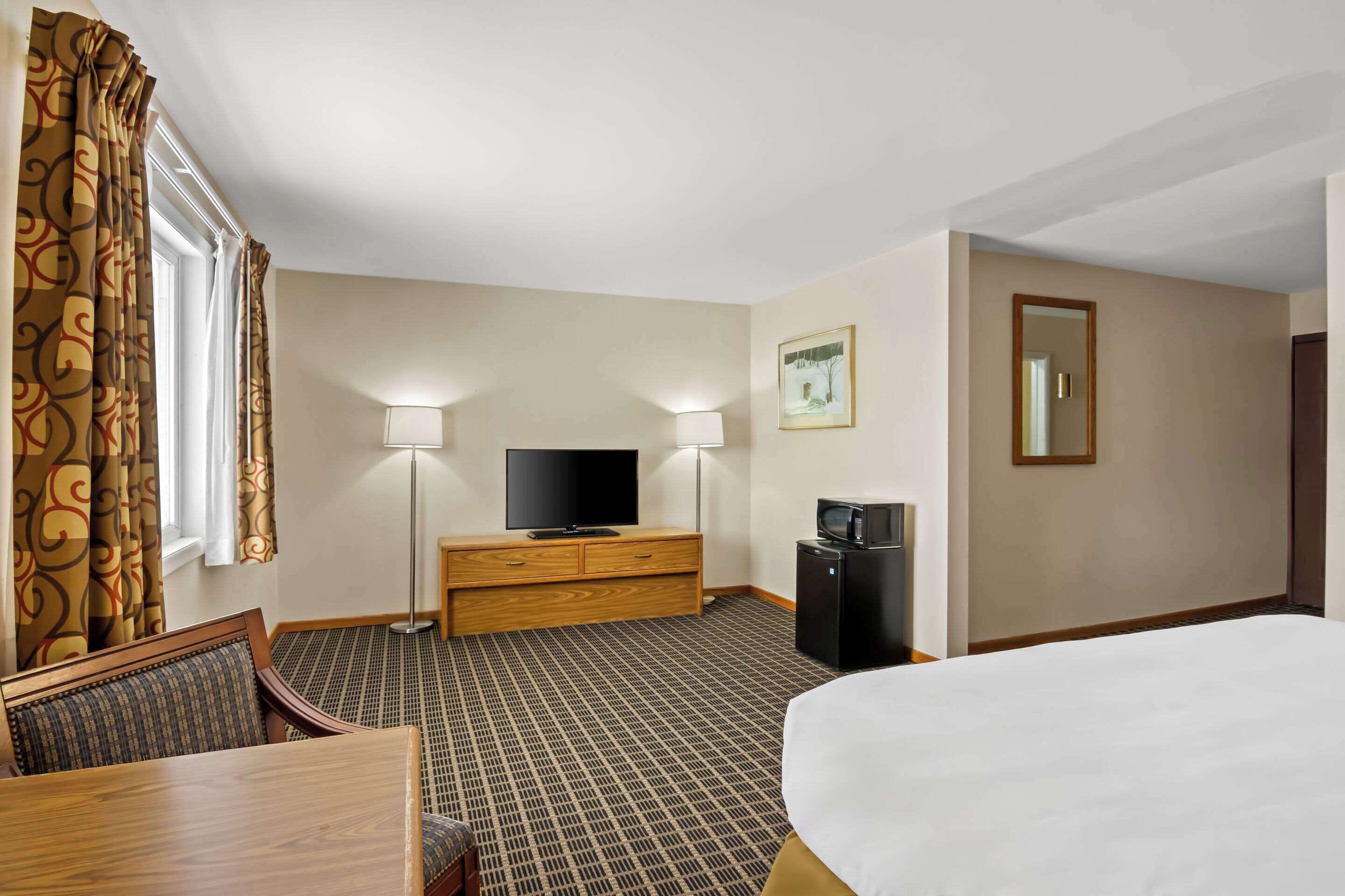 Une chambre d’hôtel équipée d’un lit, d’une télévision, d’un bureau, d’une chaise, d’une commode, d’une lampe et d’un four à micro-ondes.