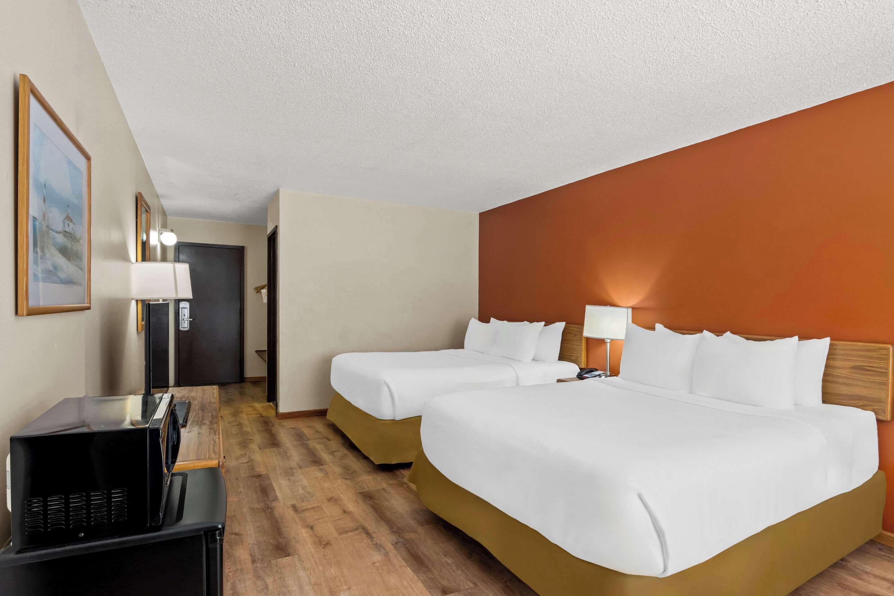 A hotel room with two beds, a desk with a computer, and a door leading to a hallway.