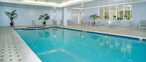 An indoor swimming pool with clear water, surrounded by lounge chairs and potted plants.