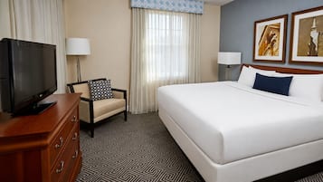 A hotel room with a bed, a television on a wooden dresser, a chair, two lamps, and two framed pictures on the wall.