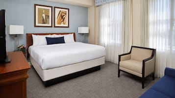 A hotel room with a king-sized bed, a chair, two wall-mounted lamps, and a television on a wooden table.