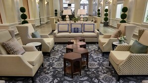 A spacious lobby with a patterned carpet, multiple seating areas including sofas and armchairs, and a piano in the background. - Hotel 24 South (Staunton)