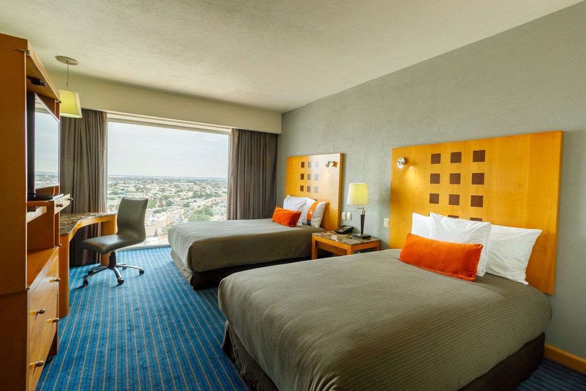Ein Hotelzimmer mit zwei Betten, einem Schreibtisch und einem Stuhl.