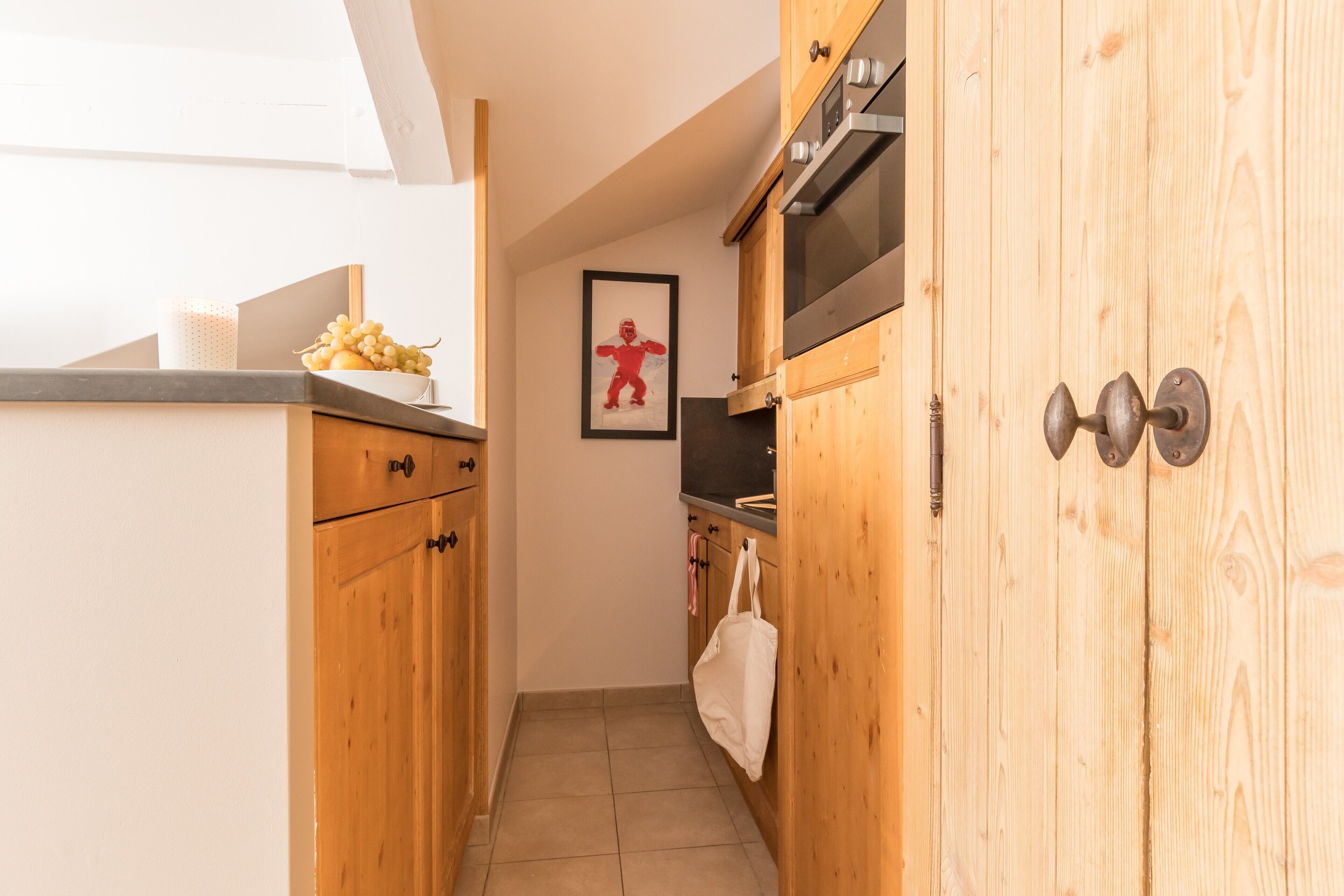 A narrow kitchen with wooden cabinets, a stainless steel oven, and a framed picture on the wall.
