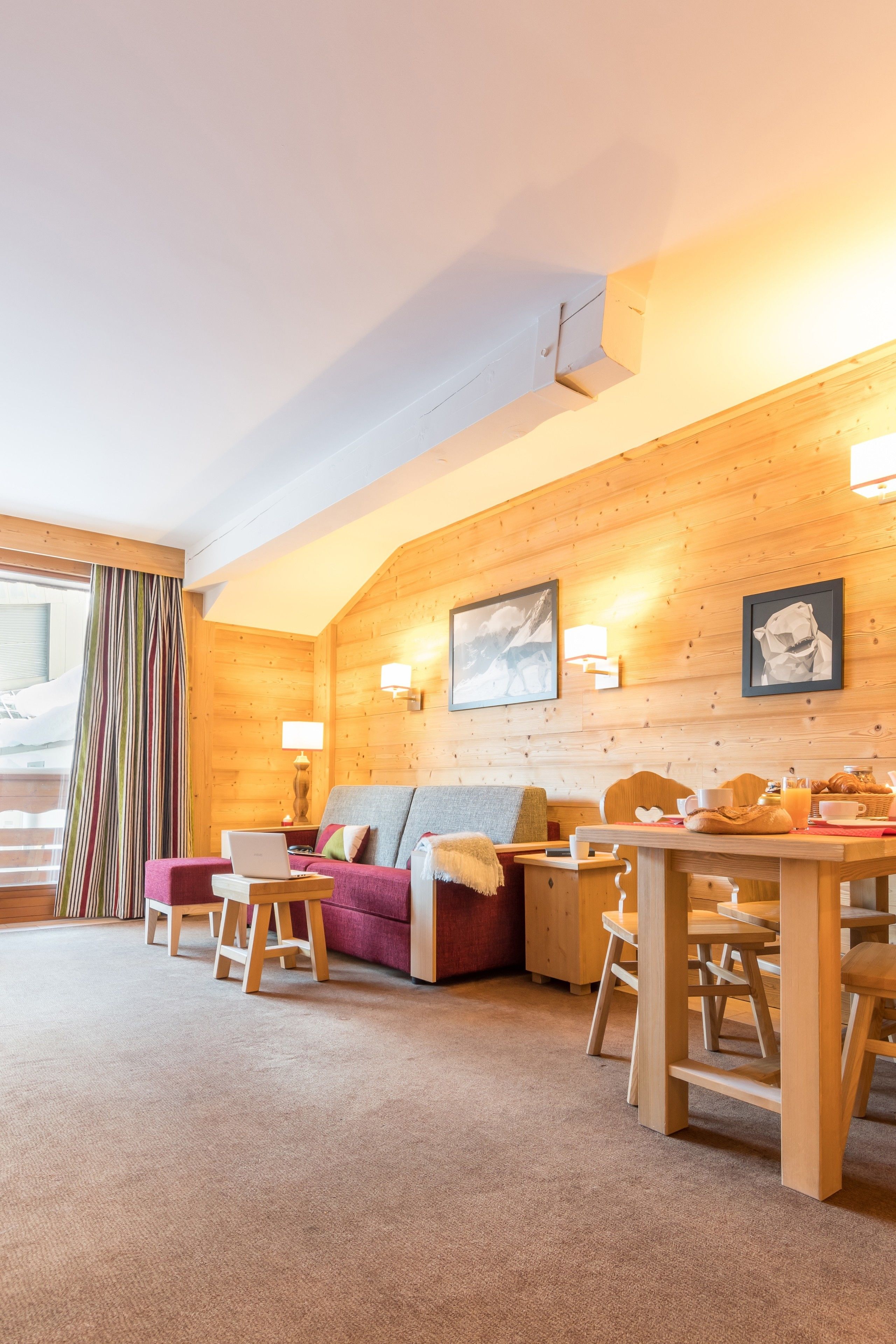 Ein gemütliches Zimmer mit Holzvertäfelung, einem Sofa, einem Tisch mit Stühlen und einem Fenster mit Vorhängen.