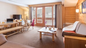 Quarto aconchegante com decoração em madeira, área de refeições com bancos, sofá, TV e mesa com vaso e bule.