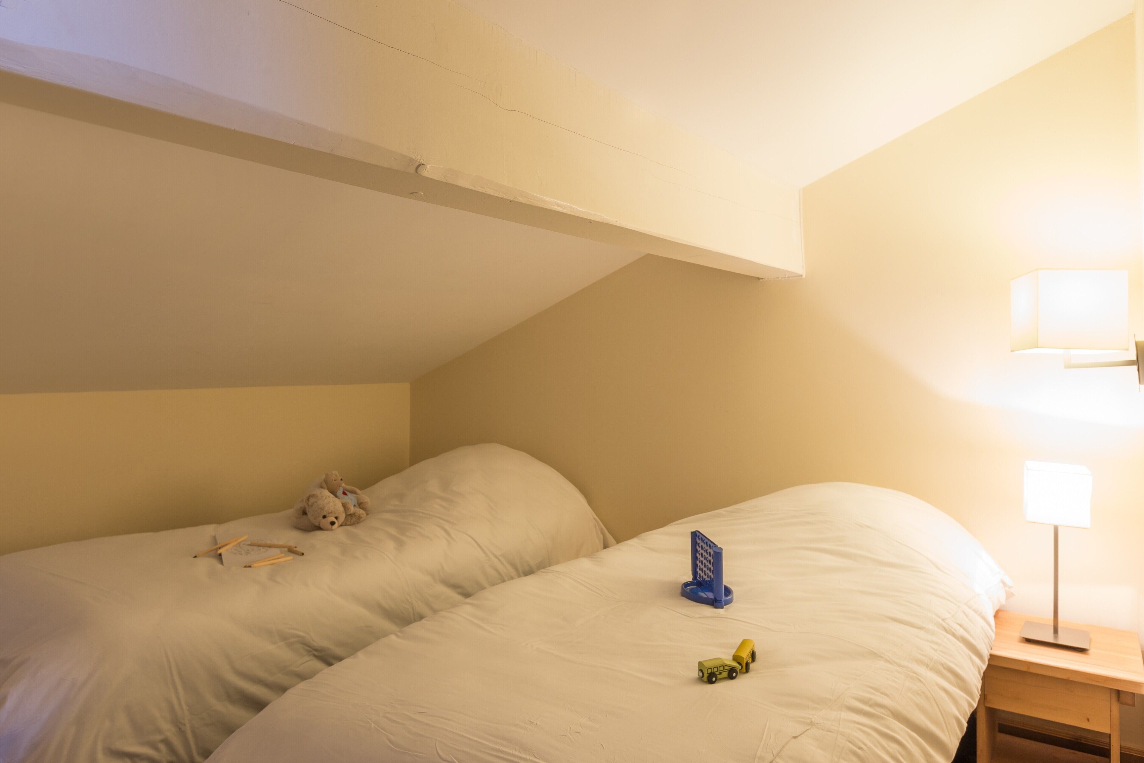 A bedroom with two beds, a nightstand with a lamp, and a teddy bear on one bed.