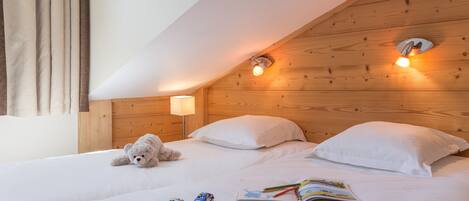 A bedroom with two beds, wooden headboard, bedside lamps, a teddy bear, and a book.