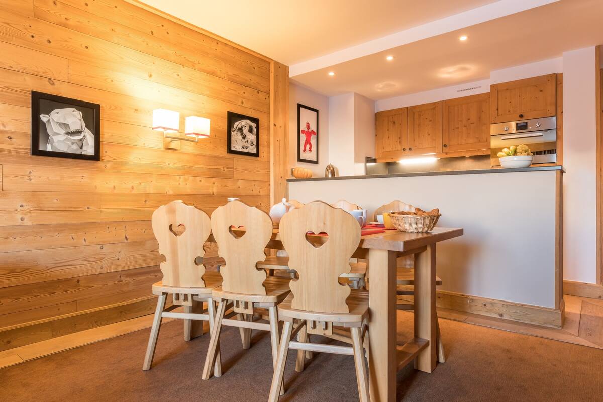 Een houten interieur met een eettafel en stoelen, houten kasten en wandlampen.