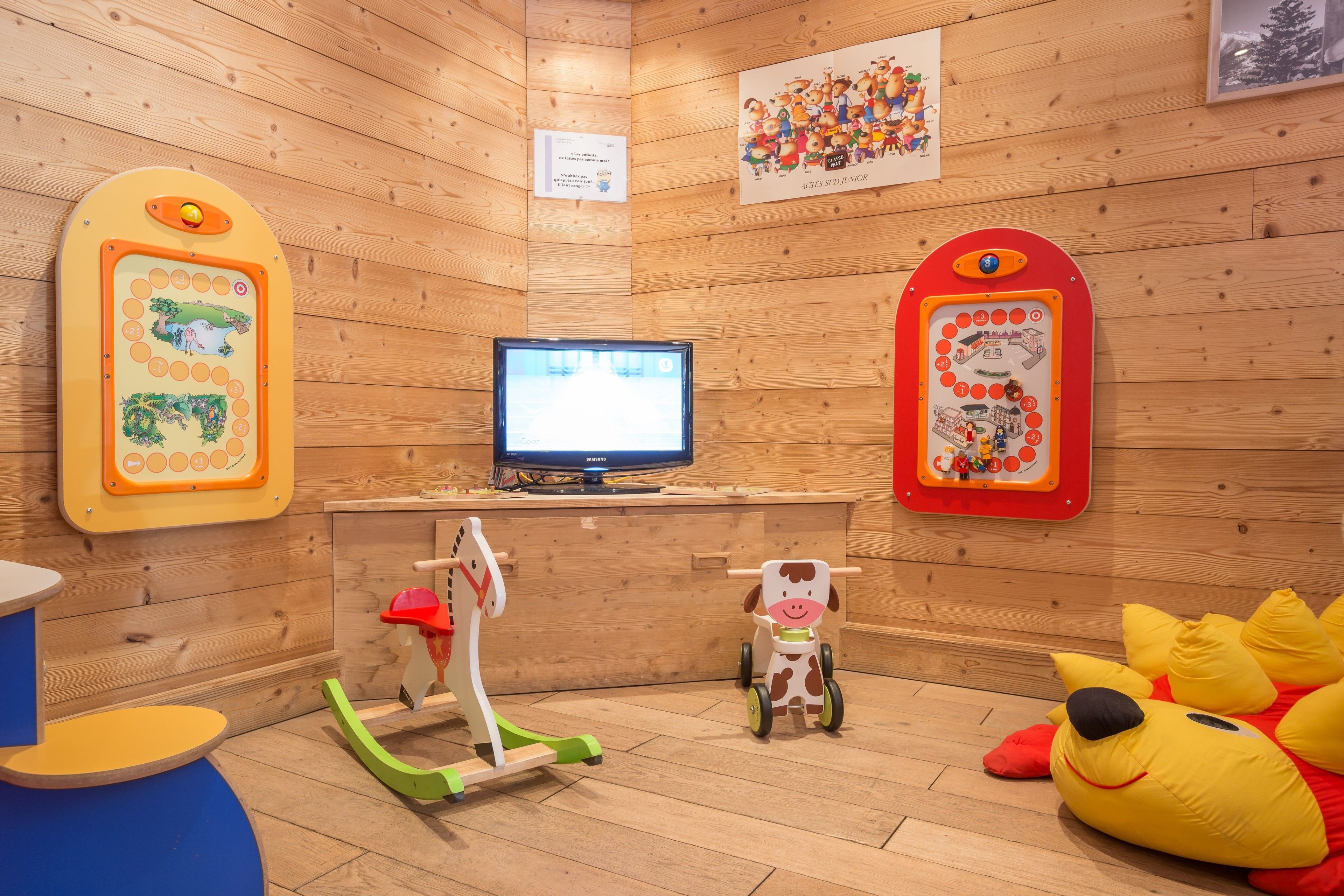 A children's play area with a television, wooden walls, and various toys.