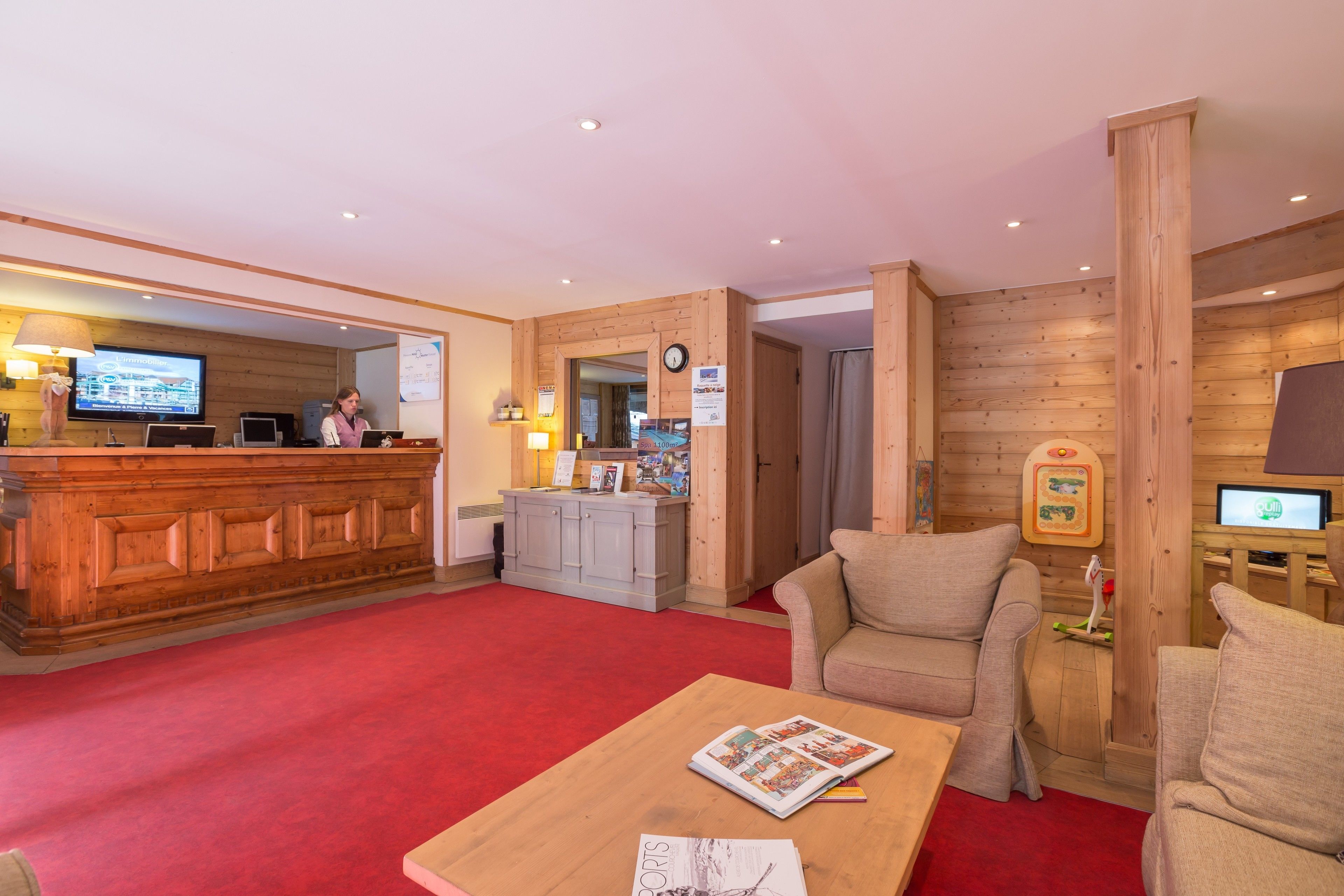 A reception area with a wooden counter, a red carpet, a sofa, and a coffee table with a magazine.
