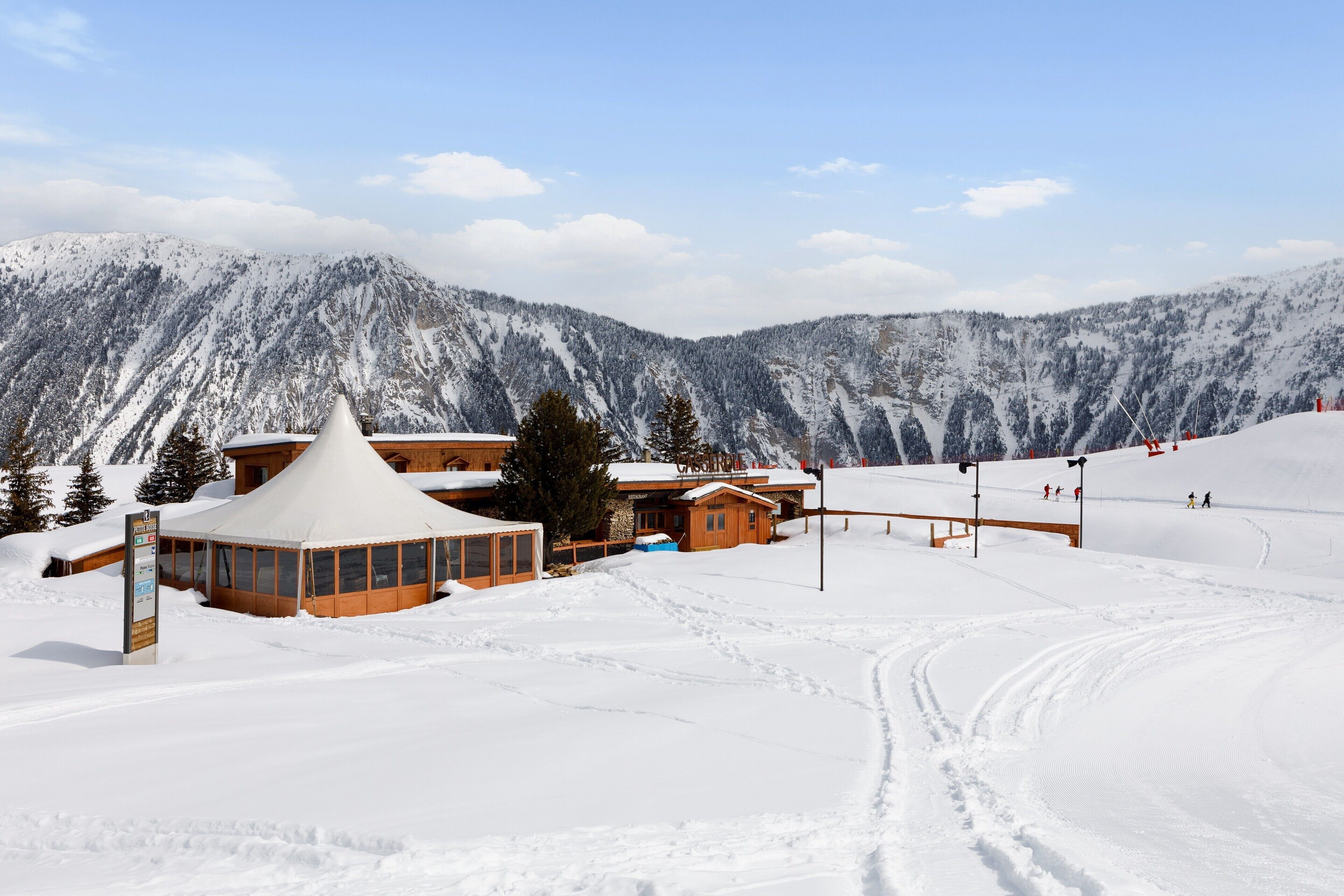 A snow-covered ski resort with a wooden lodge, a conical building, and a ski lift.
