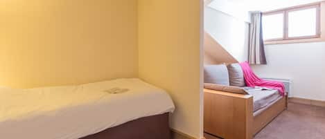 Un dormitorio con una cama individual, un banco de madera y una ventana con cortinas.