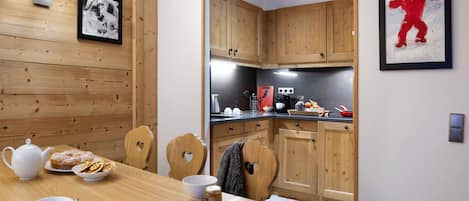 A modern kitchen with wooden cabinets, a dining table with breakfast items, and a framed artwork on the wall.