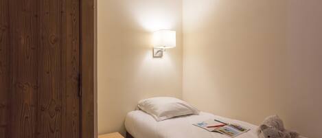 A small, neatly made bedroom with a single bed, a nightstand, a lamp, and a teddy bear.