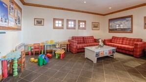 Ein Wohnzimmer mit einem rot karierten Sofa, einem weißen Couchtisch und einer Kinderspielecke mit bunten Spielsachen und Bauklötzen.