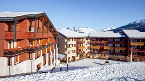 Ein Skigebiet mit mehrstöckigen Gebäuden, Skipisten und verschneiten Bergen im Hintergrund.
