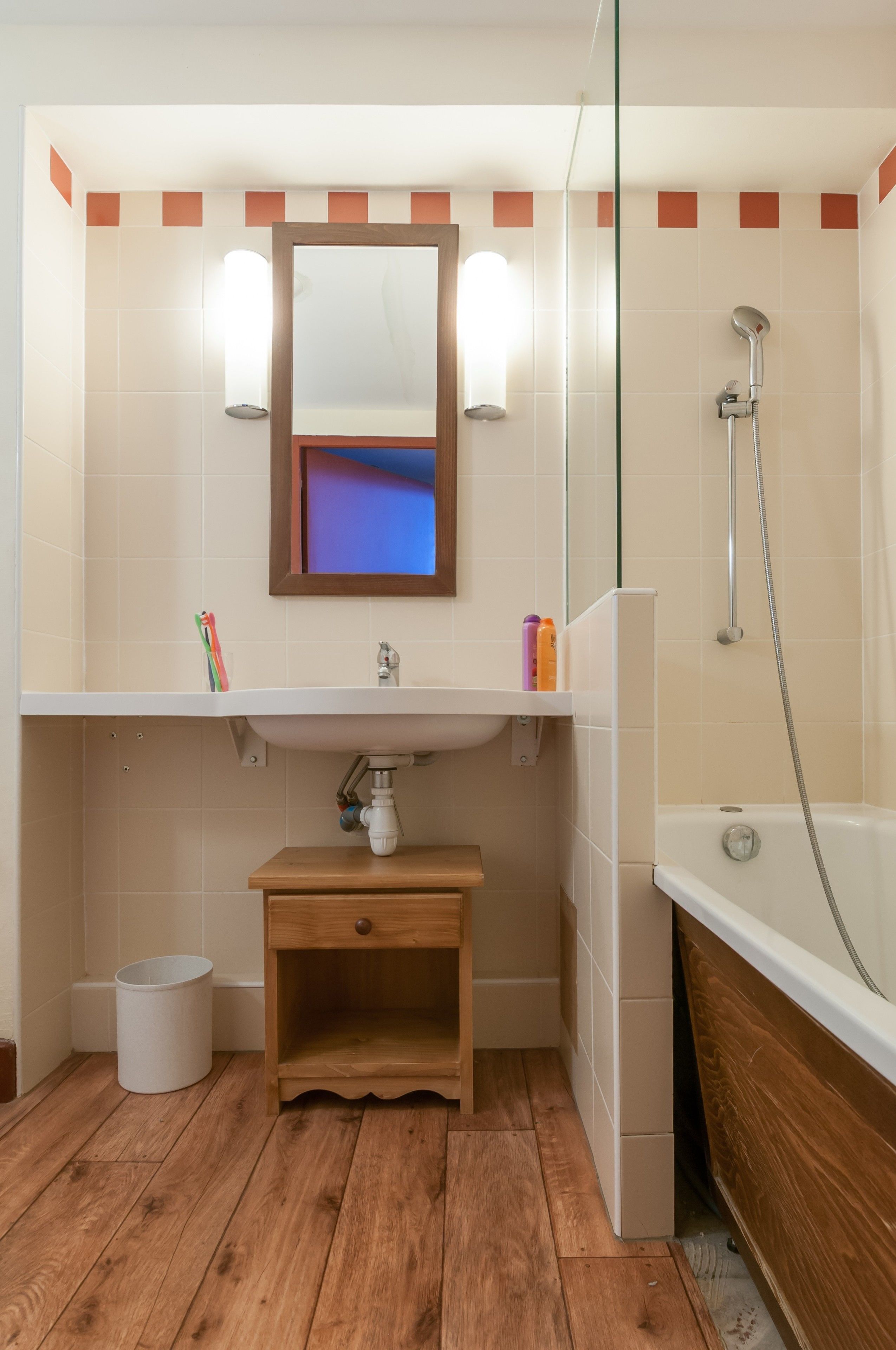 Een badkamer met een houten wastafelmeubel, een wastafel, een spiegel en een douche.