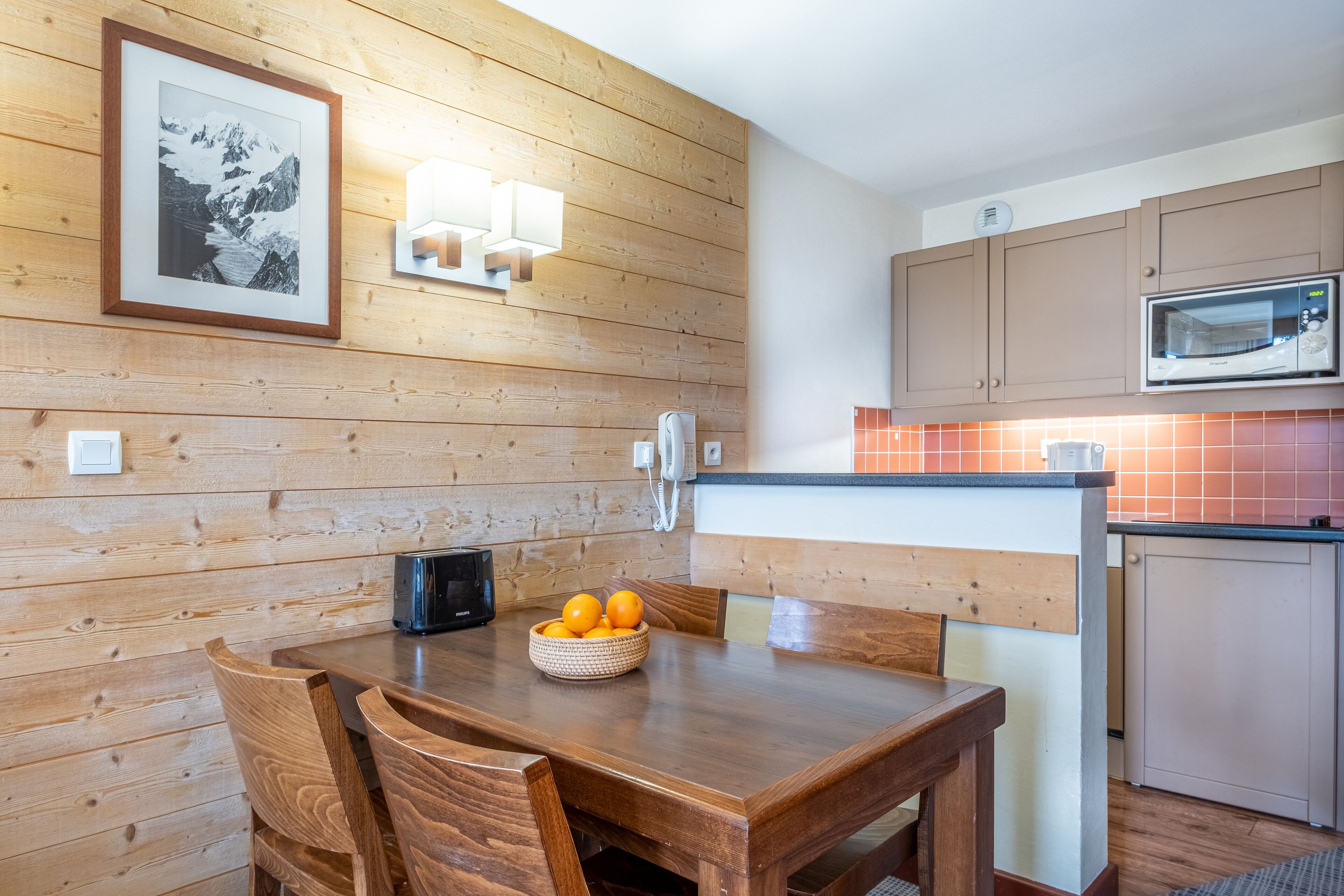 Un comedor con paneles de madera, una mesa, sillas y un cuenco de naranjas.