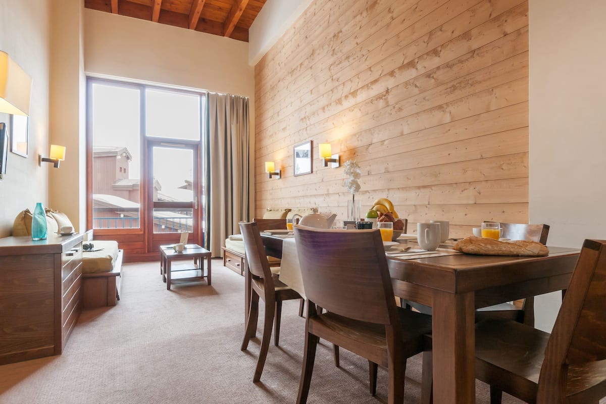 A dining area with a wooden table, chairs, and a view through a glass door to the outside.