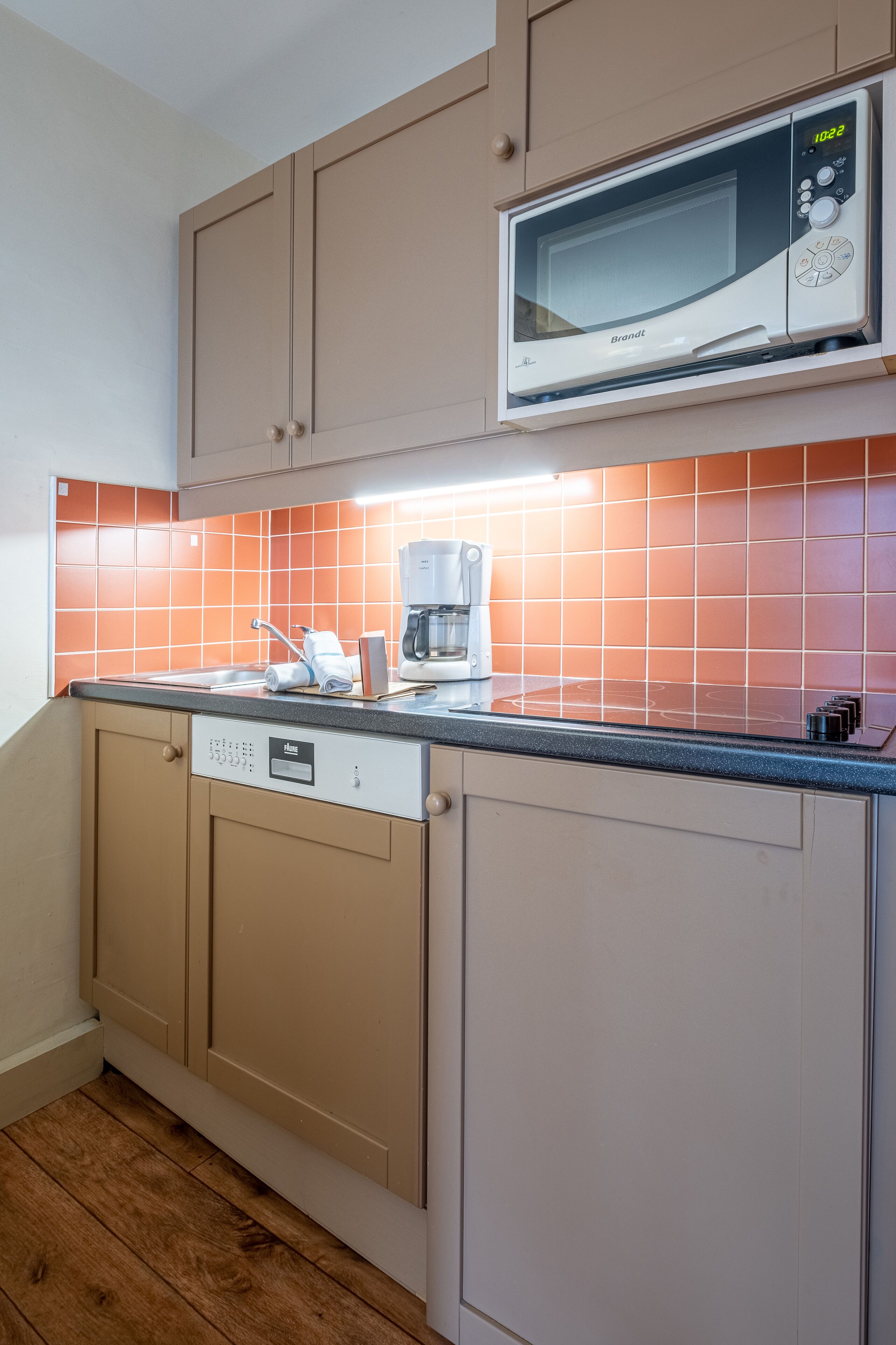 A compact kitchen with a built-in microwave, a coffee maker, and a dishwasher.
