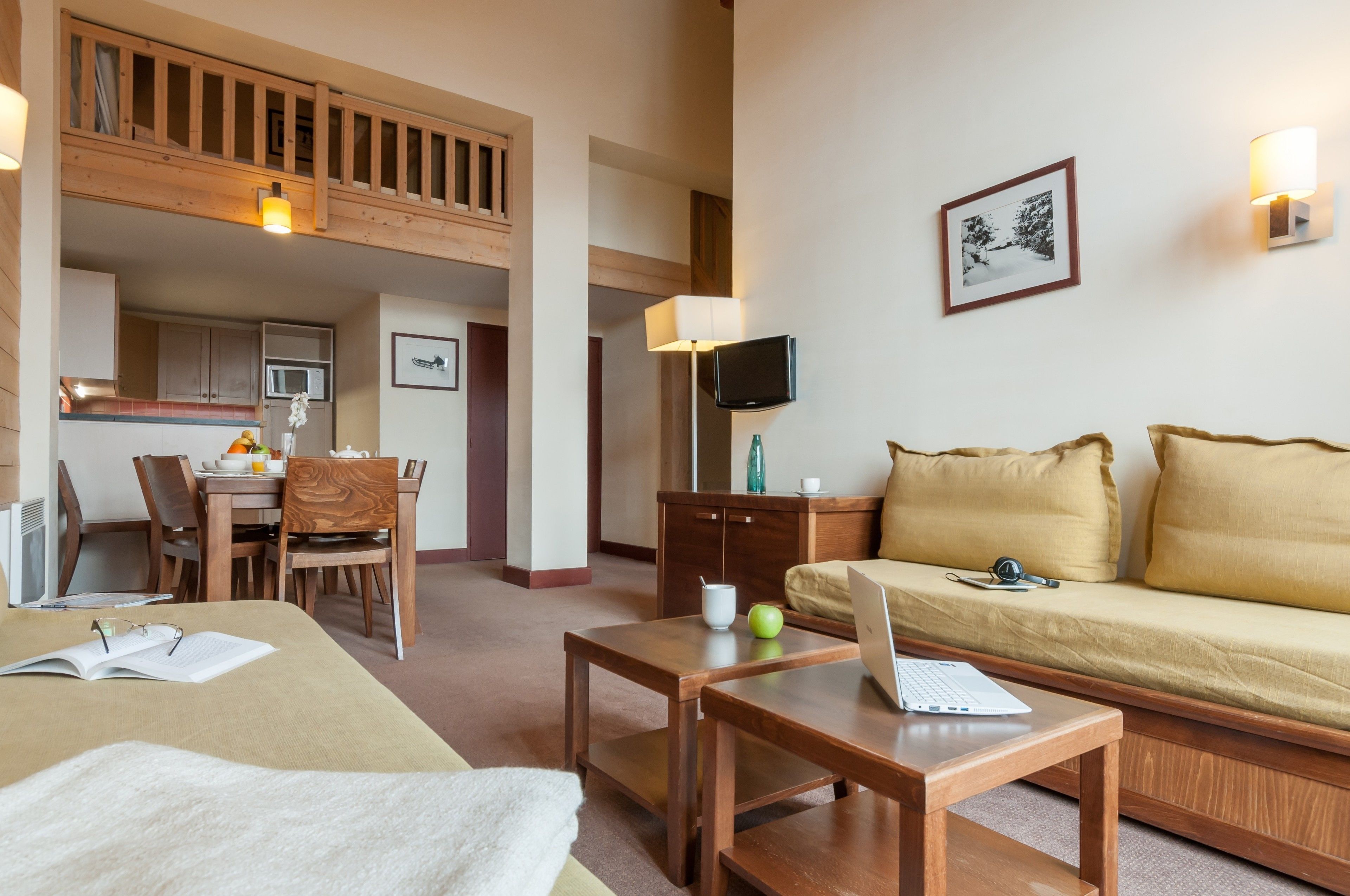 Habitación de hotel con comedor, sofá, mesa con una computadora portátil y televisor.