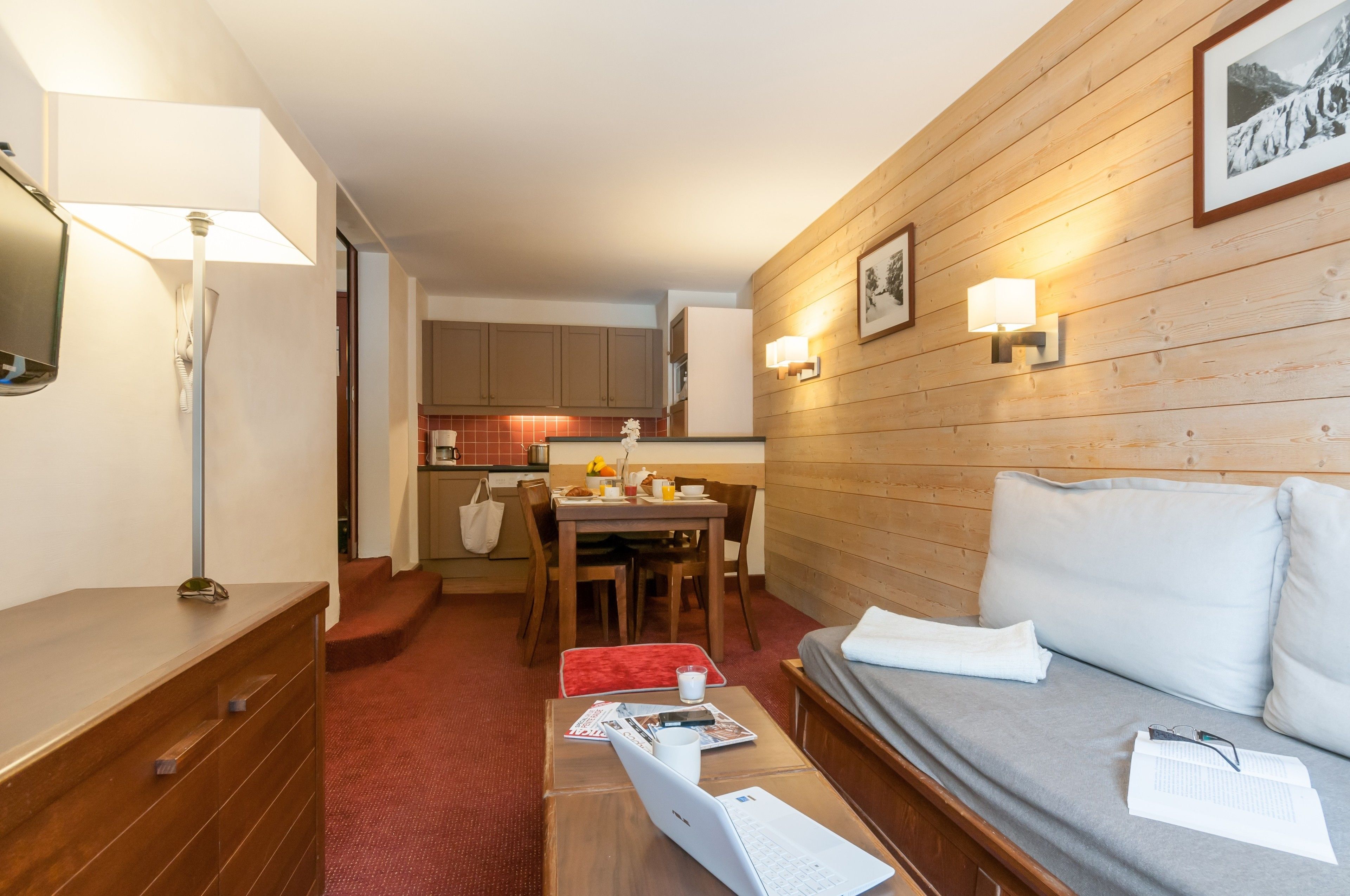 A compact room with a sofa, a small table with a laptop, a lamp, and a dining area with a table and chairs.