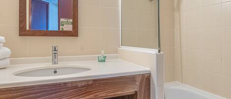 Une salle de bain avec un meuble-lavabo en bois, un évier, un miroir, une cabine de douche en verre et une baignoire.