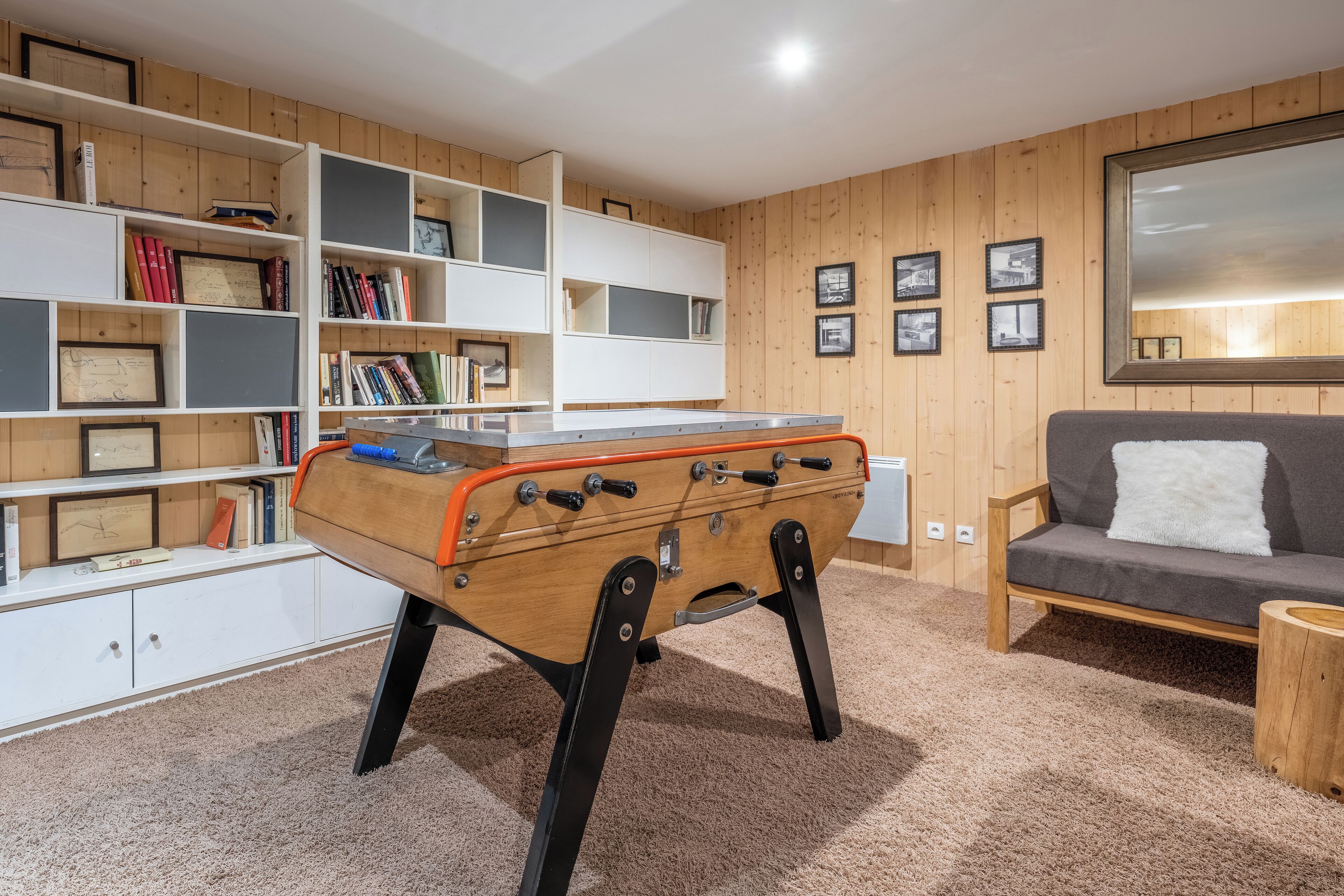 Ein gemütliches Zimmer mit Holzboden, einer Couch, einem Bücherregal und einem Billardtisch.