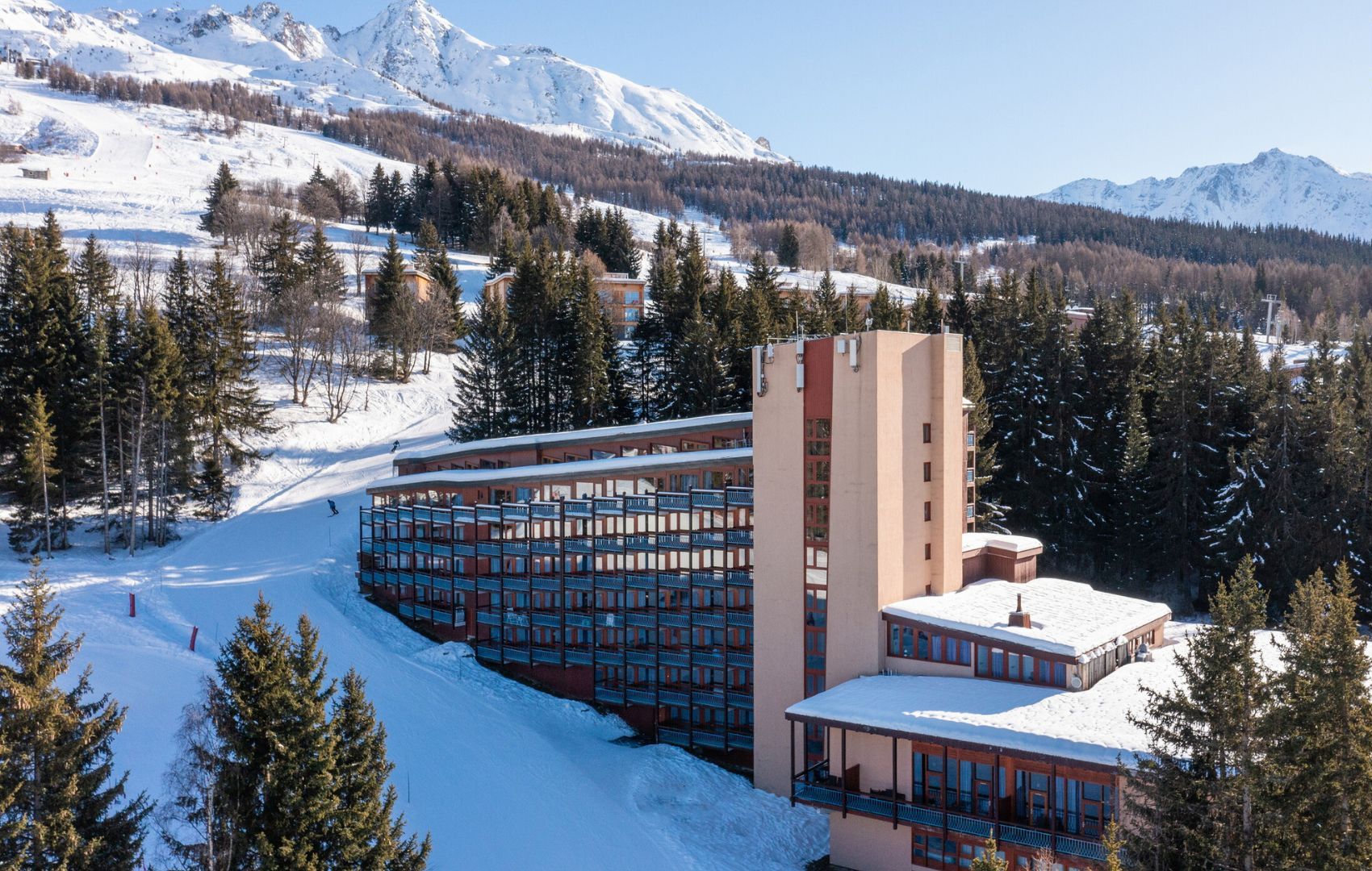 A hotel with multiple floors, a central tower, and a snow-covered landscape with mountains in the background.