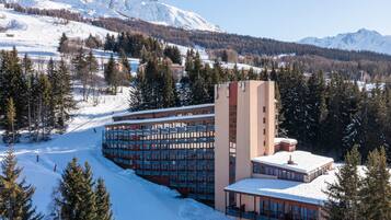 A hotel with multiple floors, a central tower, and a snow-covered landscape with mountains in the background.