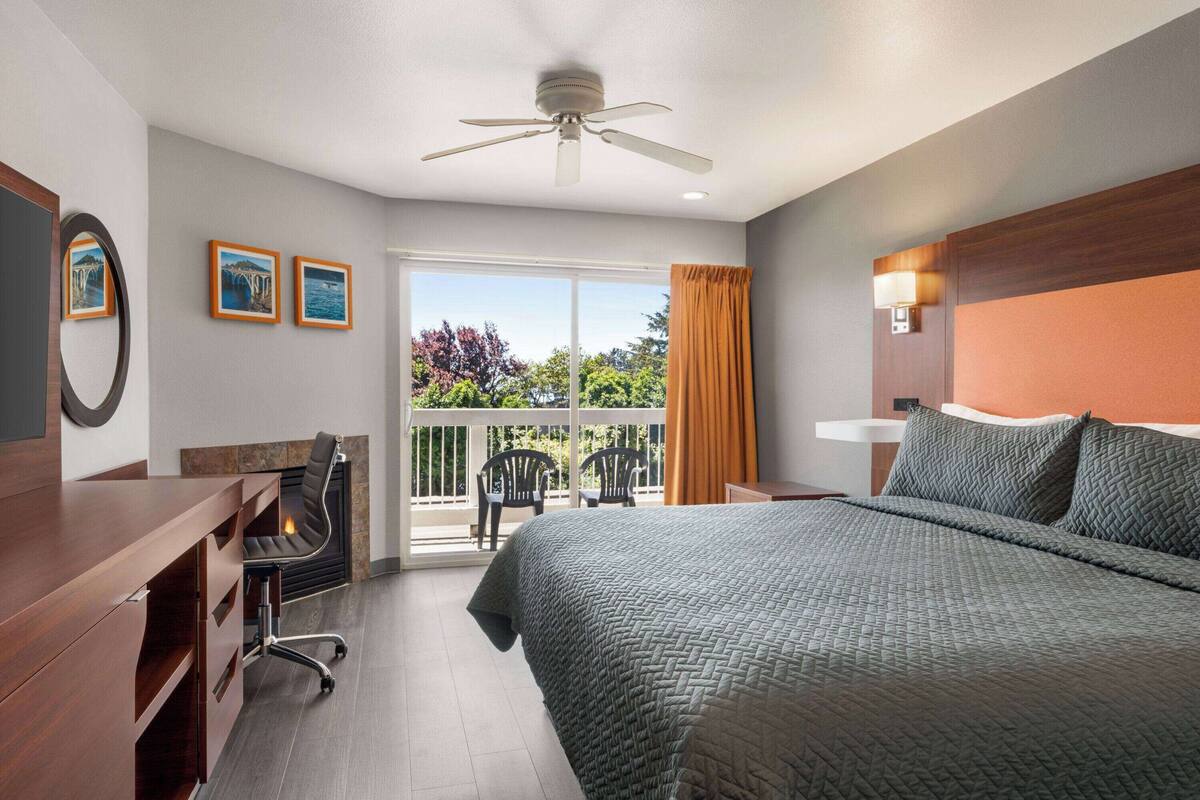 Habitación de hotel con cama, escritorio, silla, ventilador de techo y balcón con sillas.