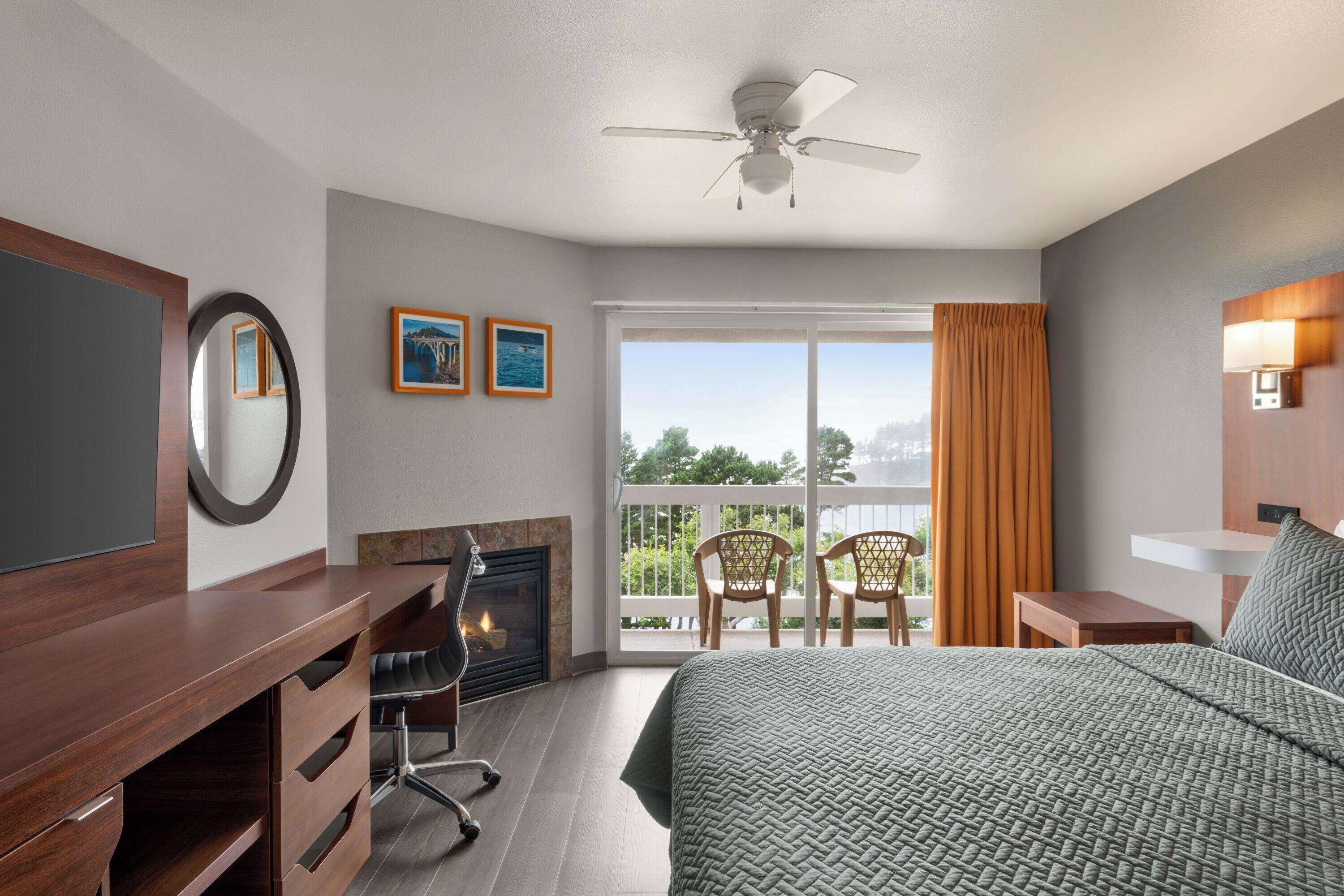 Une chambre d’hôtel comprenant un lit, un bureau, une chaise, une cheminée et un balcon avec des chaises.
