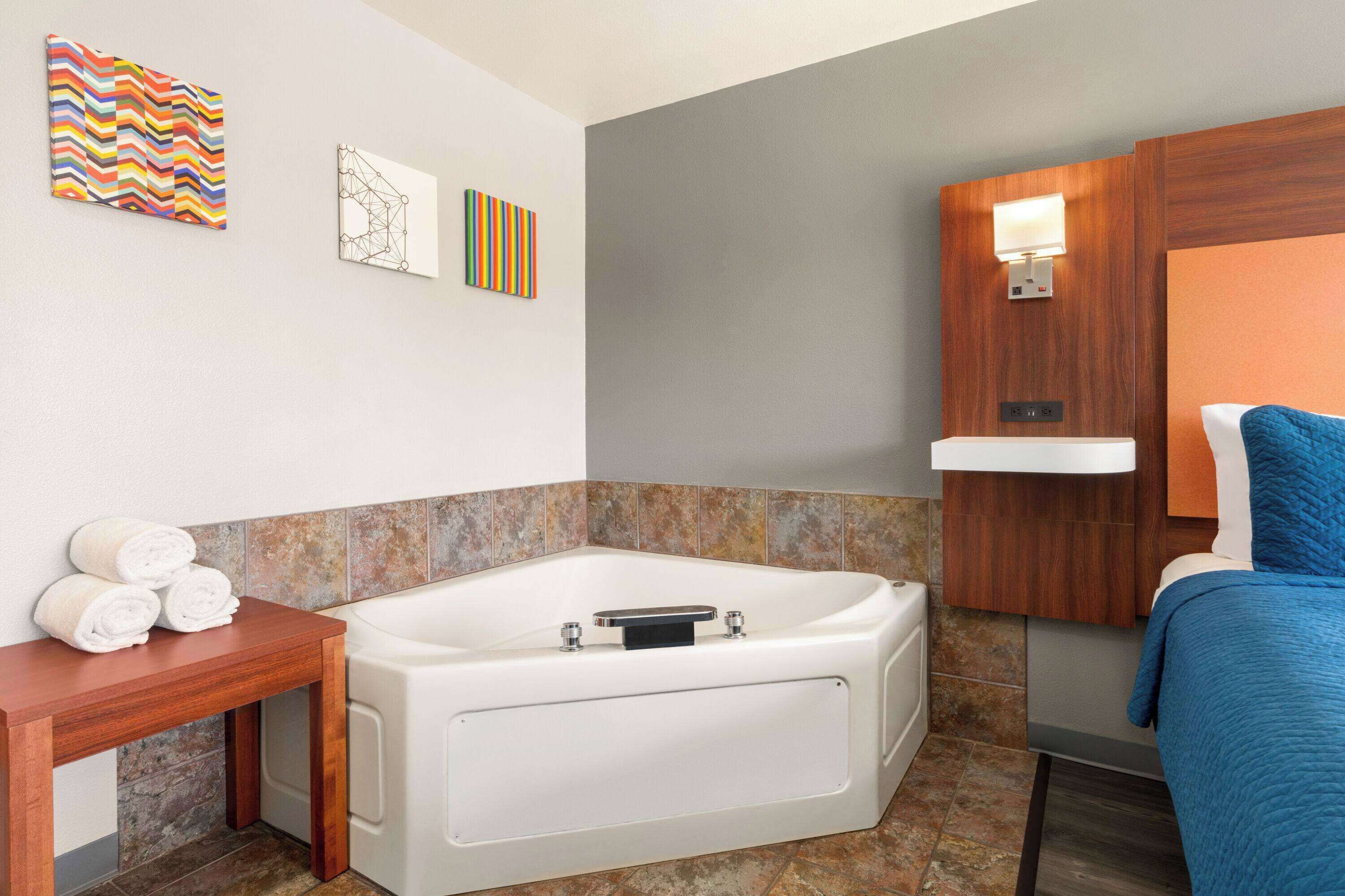 Un baño moderno con una bañera, una mesita de madera con toallas y obras de arte en la pared.