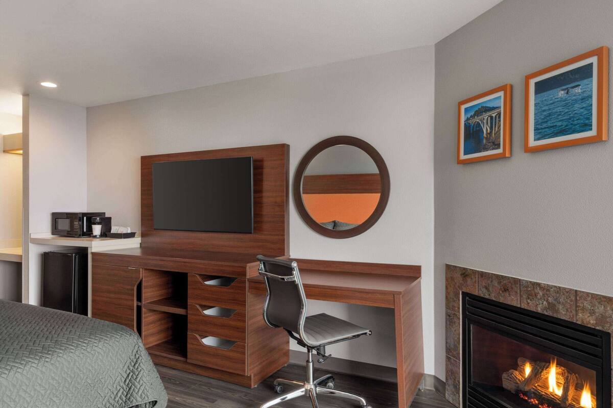 Habitación de hotel con televisor de pantalla plana, chimenea, escritorio con silla, cama y dos cuadros en la pared.