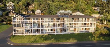 Un hotel de varios pisos con balcones, situado en una zona residencial con casas y árboles al fondo.