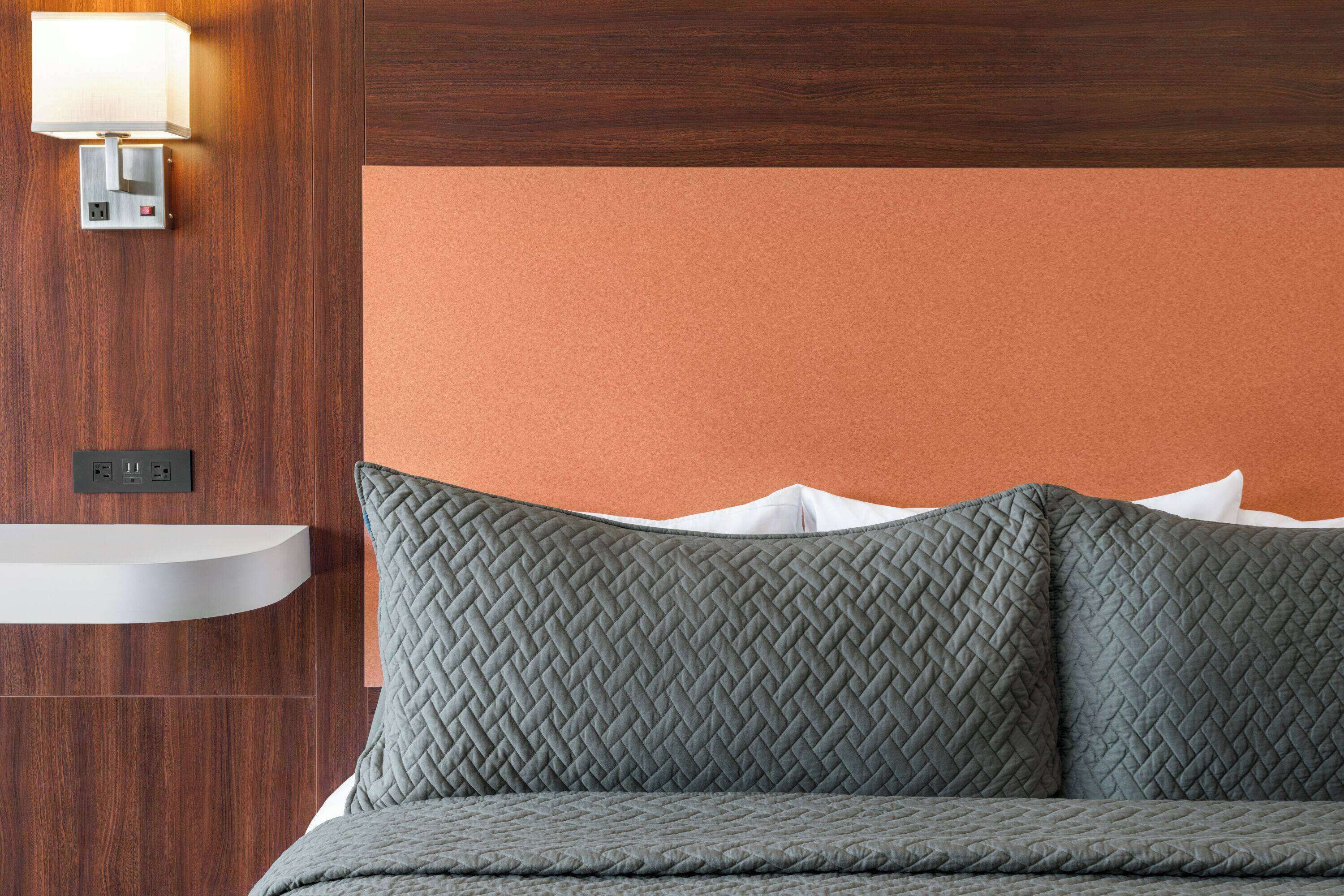 Una cama con cabecera acolchada, una lámpara de pared y un panel de madera.