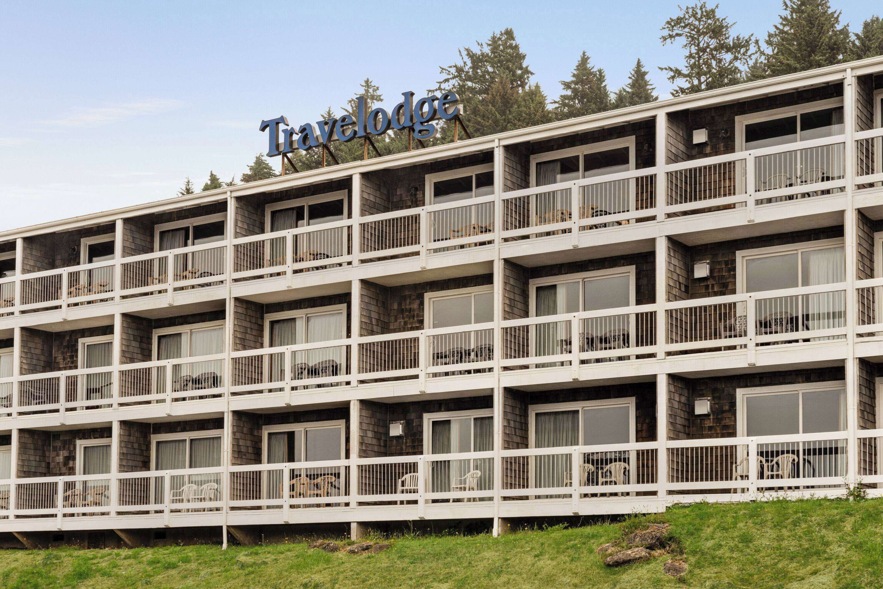 Un edificio de varios pisos con balcones, un letrero que dice 'Travelodge' y un área verde al frente.