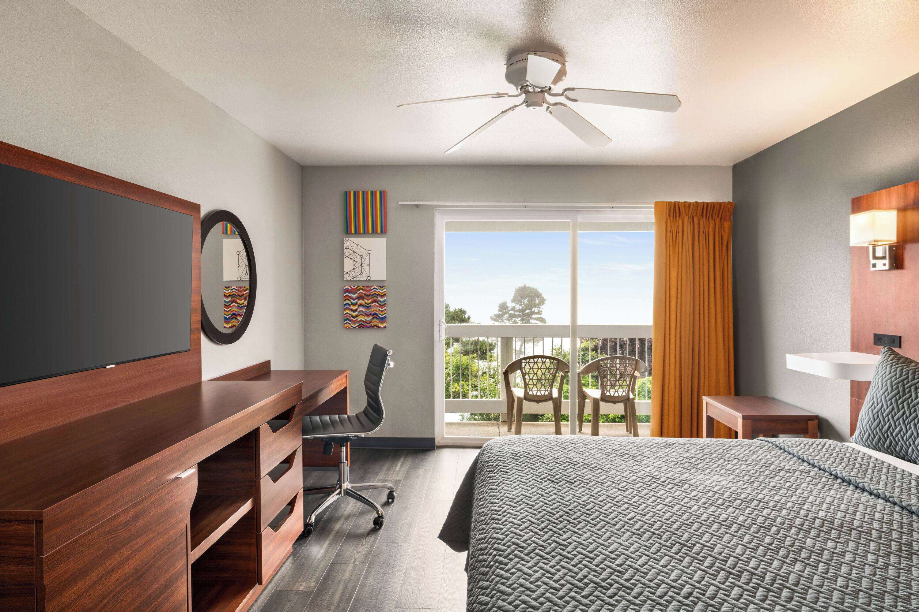 A hotel room with a bed, a desk, a chair, a television, and a balcony with a view.