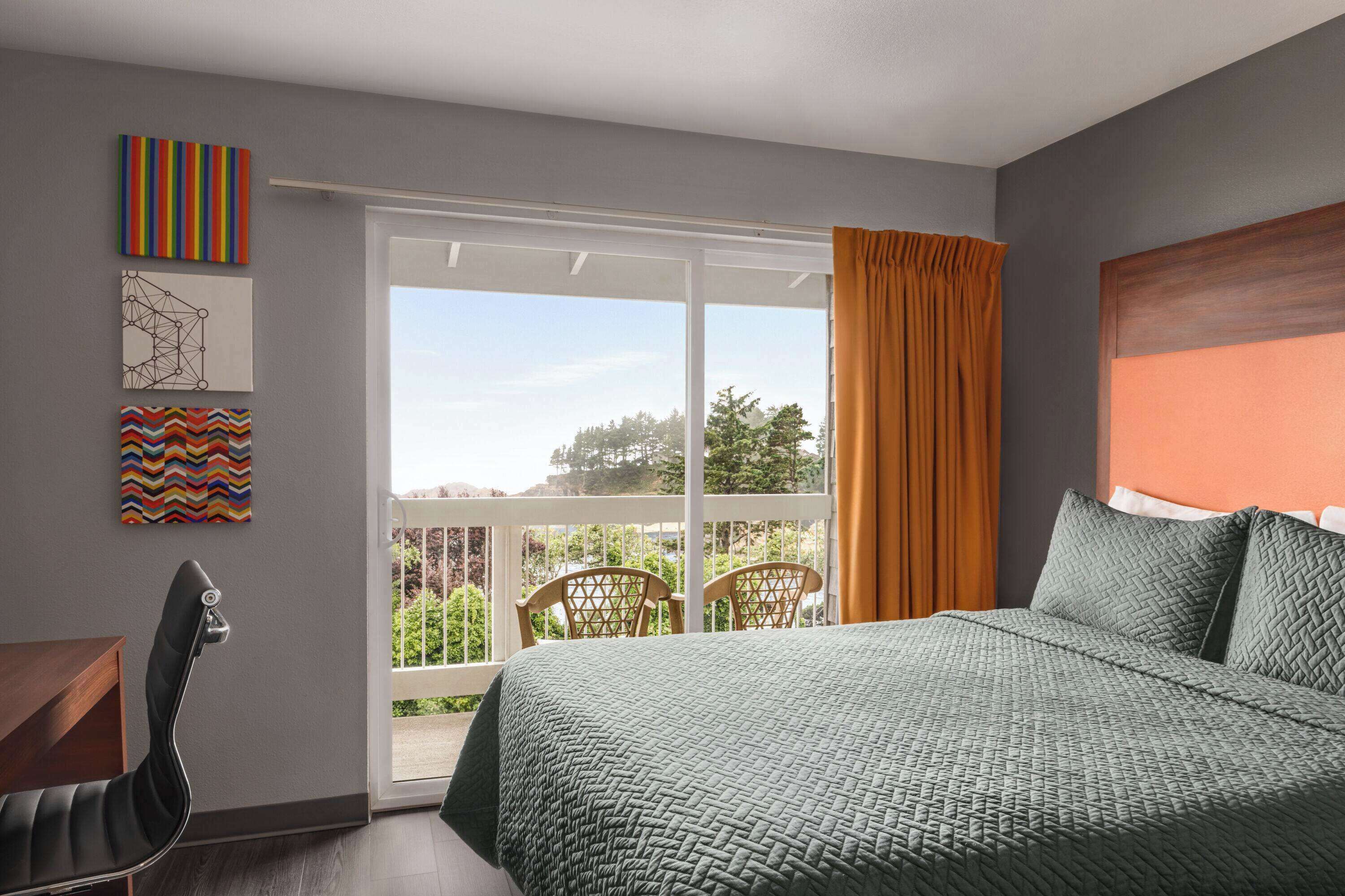 A bedroom with a bed, a desk, chairs, and a balcony with a view.